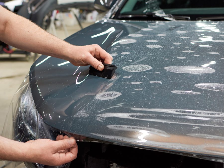 Installation of a protective paint and varnish transparent film on the car. PPF polyurethane film to protect the car paint from stones, marks and scratches.